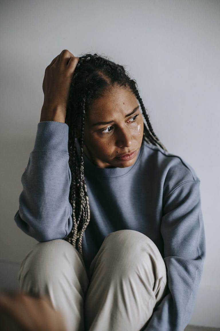 Mournful nervous African American female in casual wear crying on floor while embracing knees and looking away