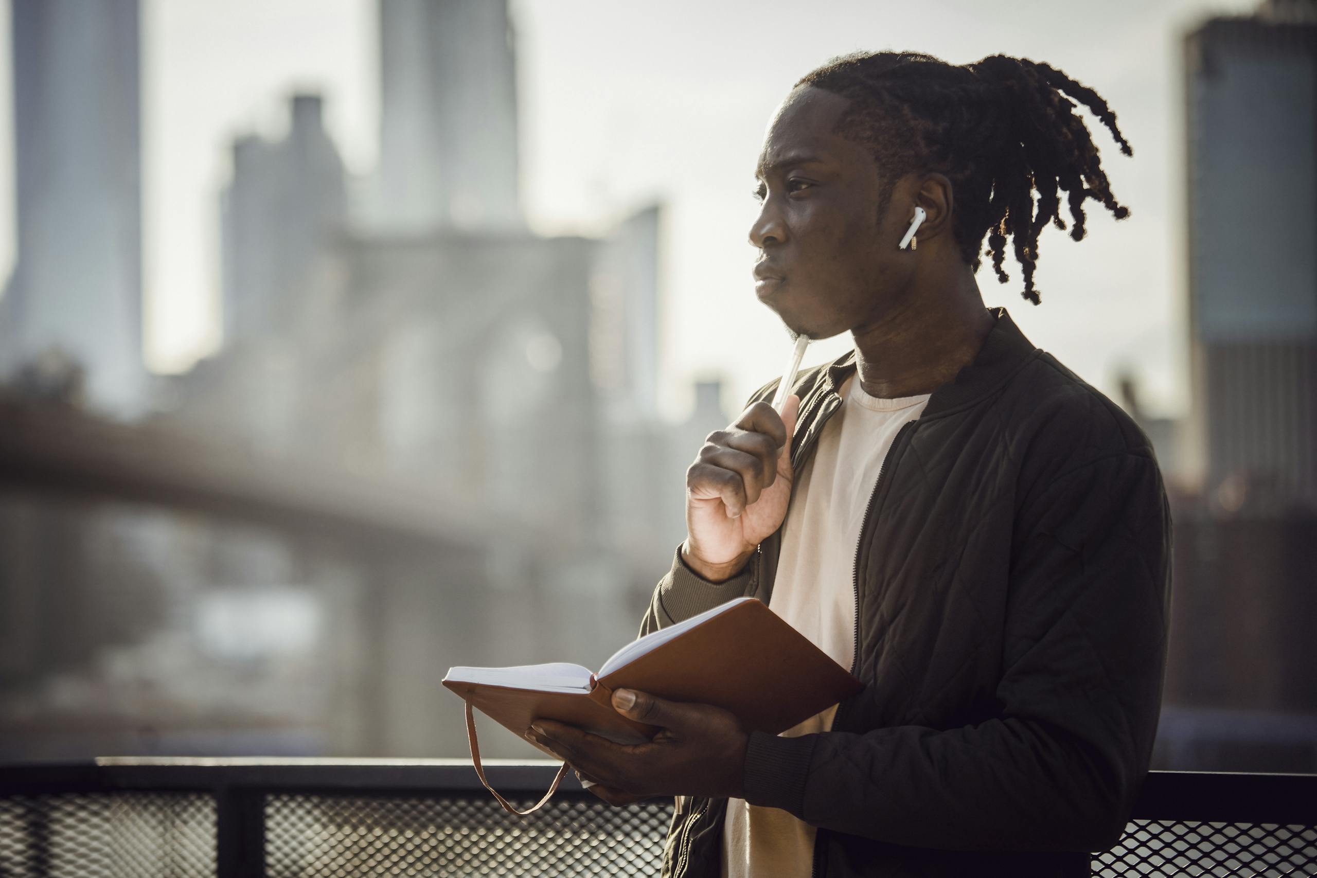 Thoughtful black man in wireless earphones with notepad on balcony