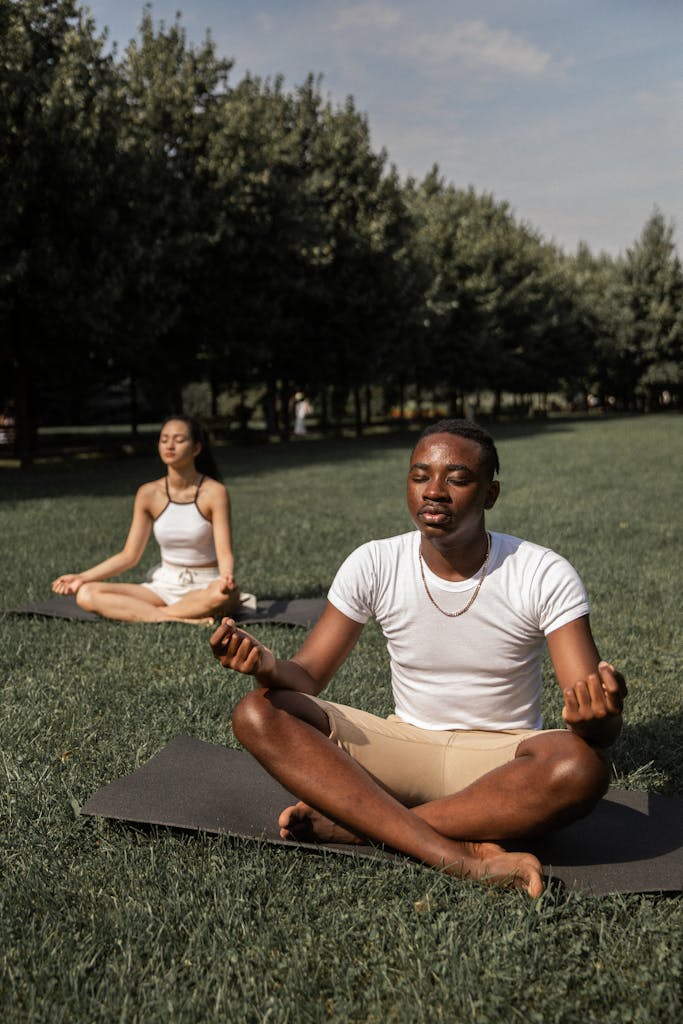 Full body of flexible barefoot couple in activewear sitting on mats in Lotus pose with closed eyes while practicing yoga together