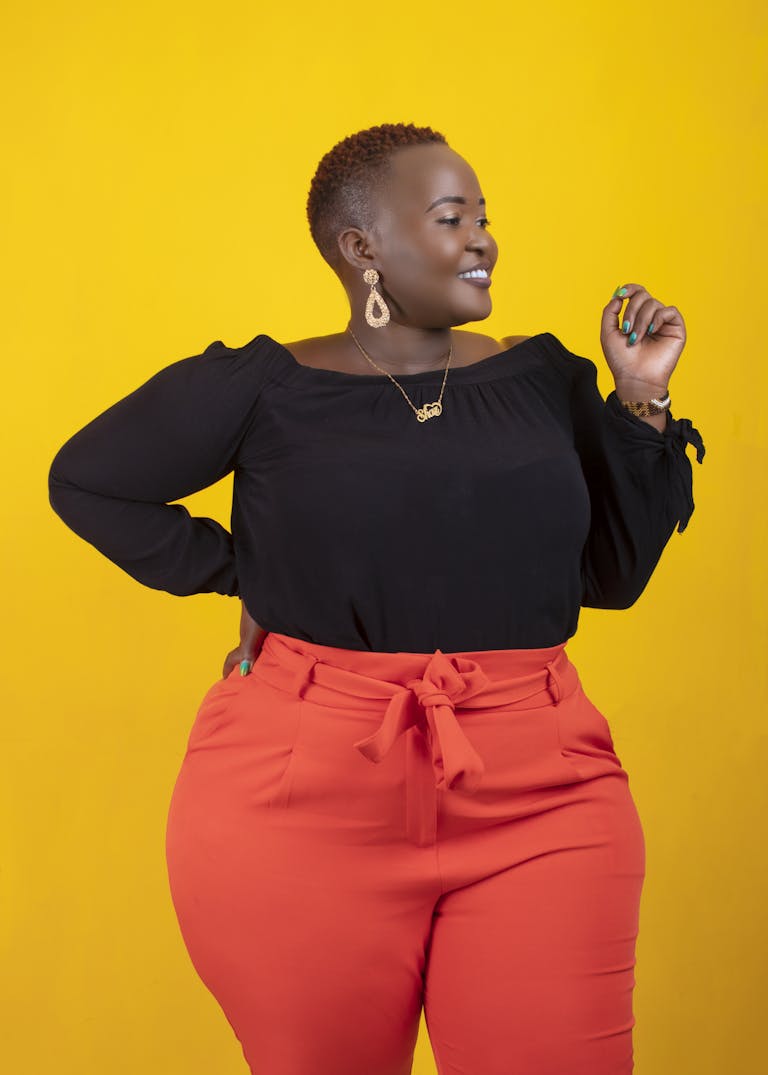 Young positive African American plus size female with hand on waist standing against bright yellow background and looking away