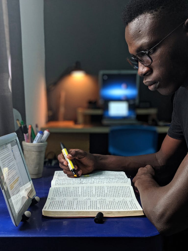 Man deeply engaged in studying with a book and tablet at a desk