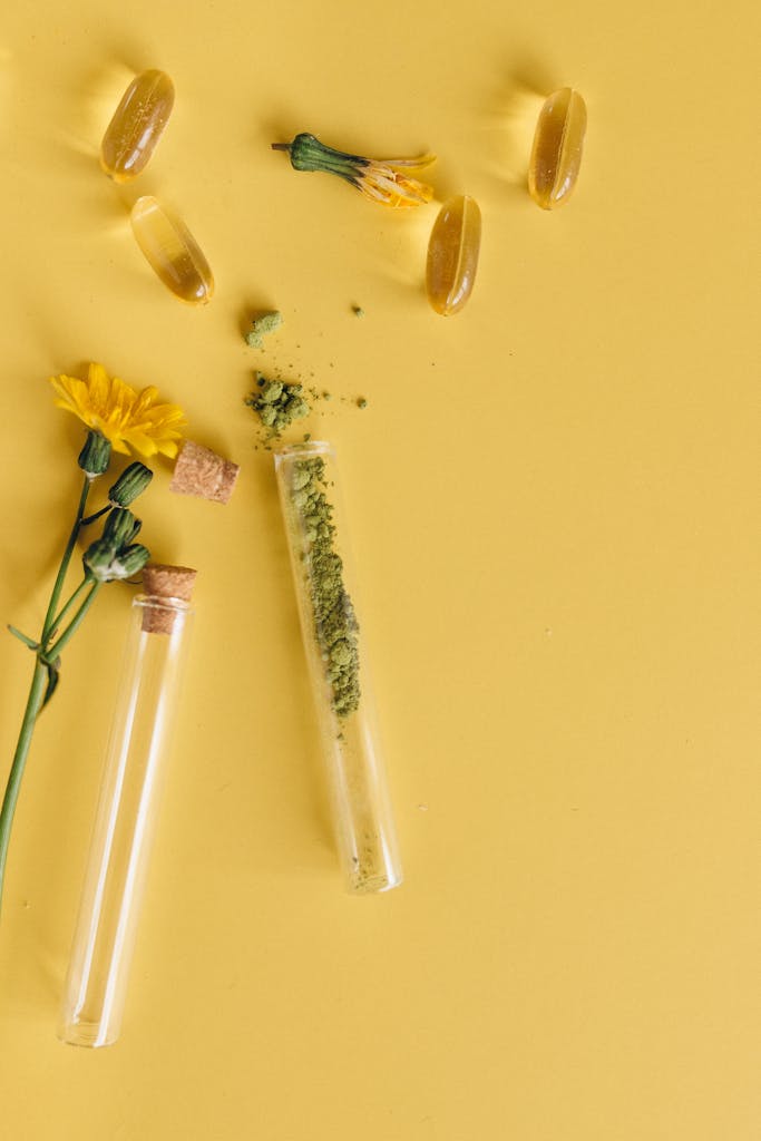 Top view of herbal capsules and flowers with test tubes on a vibrant yellow surface.