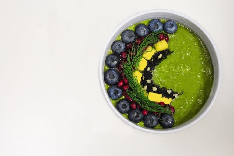 A vibrant green smoothie bowl decorated with blueberries and garnishes for a healthy breakfast.