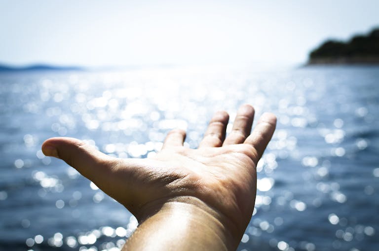 A hand reaching towards the sparkling sea, symbolizing freedom and hope.