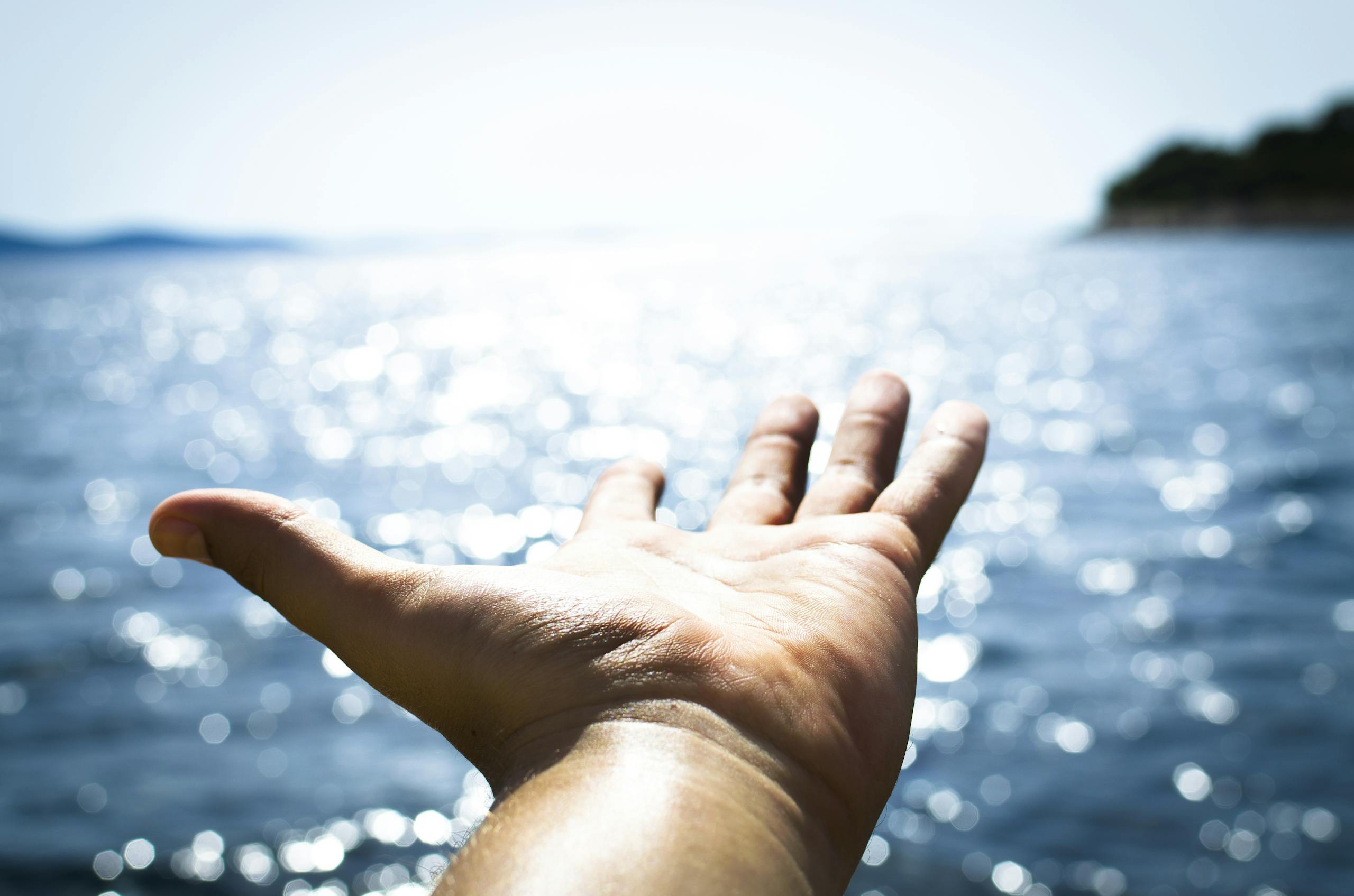 A hand reaching towards the sparkling sea, symbolizing freedom and hope.