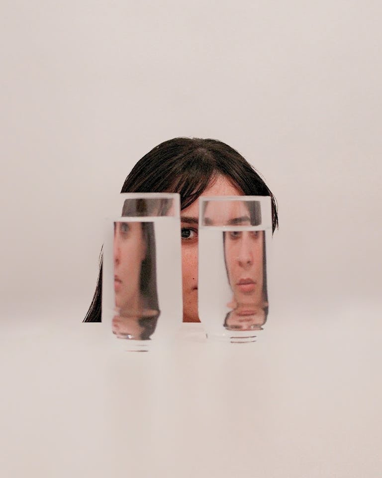 Surreal portrait of a woman with her face reflected through glasses of water, creating intriguing visual distortion.