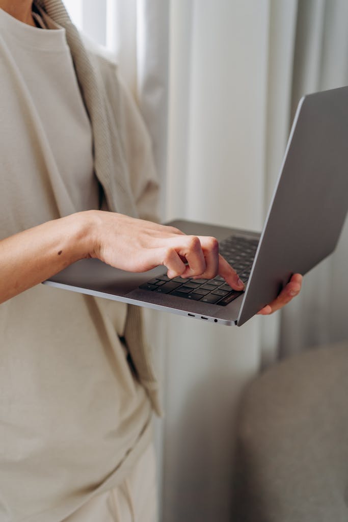 Close-up of a person typing on a wireless laptop in an indoor setting.